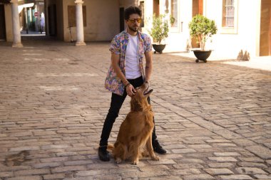 young latin man with sunglasses and beard and his brown golden retriever dog walking in the streets of a big european city. Concept pets, animals, dogs, love to retriever pets.
