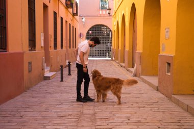 young latin man with sunglasses and beard and his brown golden retriever dog walking in the streets of a big european city. Concept pets, animals, dogs, love to retriever pets.