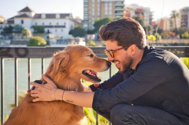 young latino man with sunglasses and beard and his brown golden retriever dog look at each other with love and affection. Concept pets, animals, dogs, love to retriever pets.