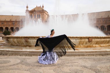 Dişi flamenko dansçısı, genç esmer ve güzel tipik İspanyol dansçı Seville Meydanı 'ndaki bir fıskiyenin önünde siyah bir şalla dans ediyor. Flamenko dünya kültür mirası konsepti.