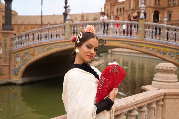 Beautiful teenage flamenco dancer with brunette hair and dressed in dance clothes makes different postures and expressions with a red fan while covering her face. Language of the fan.