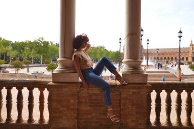 Güzel bir kadın Seville 'i geziyor, kadın Sevilla' nın en büyük ve en ünlü meydanında iki sütunun arasında oturuyor. Kadın çok mutlu. Tatil ve seyahat kavramı.
