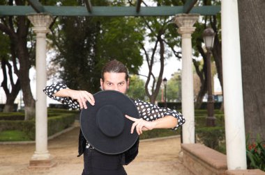 Çingene adam uzun saçlı ve sakallı flamenko dansı yapıyor mermer sütunların yanındaki parkta. Elinde siyah bir şapka tutuyor ve tutkuyla farklı duruşlar sergiliyor. Flamenko dansı.