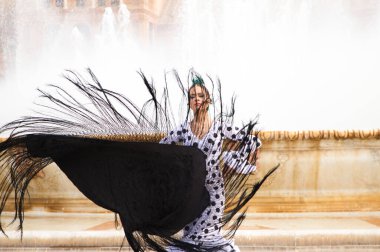 Dişi flamenko dansçısı, genç esmer ve güzel tipik İspanyol dansçı Seville Meydanı 'ndaki bir fıskiyenin önünde siyah bir şalla dans ediyor. Flamenko dünya kültür mirası konsepti.