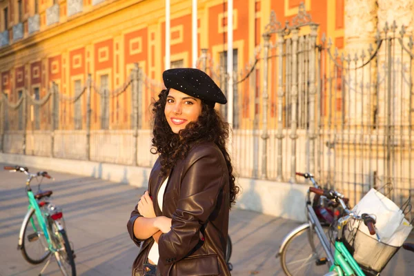 Kameraya doğru kıvırcık saçlı, siyah saçlı genç ve güzel bir kadın. O bir anıtın önünde geziyor ve arka planda bir bisiklet görebilirsiniz. Tatil ve turizm konsepti.