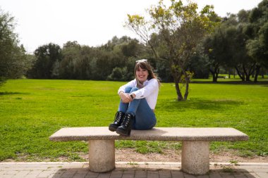 Güzel, sarışın, genç bir kadın bankta oturmuş farklı pozlar ve ifadeler veriyor. Kadın, şehirde tatilde. Seyahat ve tatil konsepti.