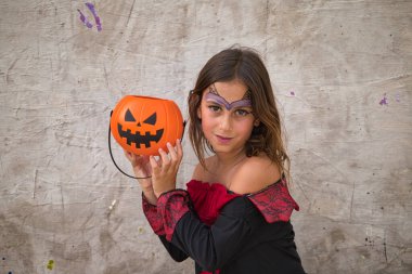 Happy halloween. Cute little girl dressed up as a witch for halloween party on grey background and pumpkin in her hand. Trick or treat.