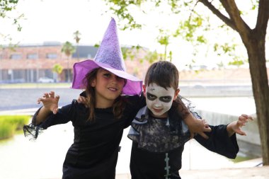 Happy halloween. A girl dressed as a witch with a hat and a boy dressed as a zombie have fun at the halloween party in the park. The children pose for a photo. Trick or treat. 31st October.