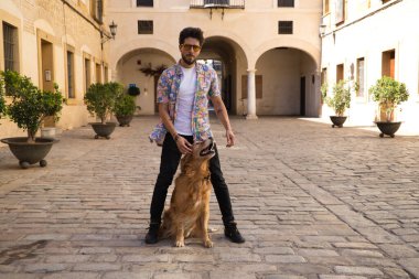 young latin man and his brown golden retriever dog, the man standing up looks at his pet who is sitting on the ground and grabs his head. Pets concept.