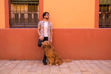 young latin man and his brown golden retriever dog, the man standing up looks at his pet who is sitting on the ground and grabs his head. Pets concept.