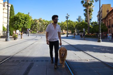 young latin man with sunglasses and beard and his brown golden retriever dog walking in the streets of a big european city. Concept pets, animals, dogs, love to retriever pets.