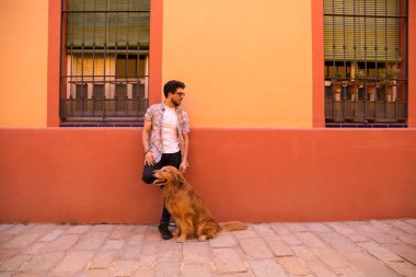 young latin man and his brown golden retriever dog, the man standing up looks at his pet who is sitting on the ground and grabs his head. Pets concept.