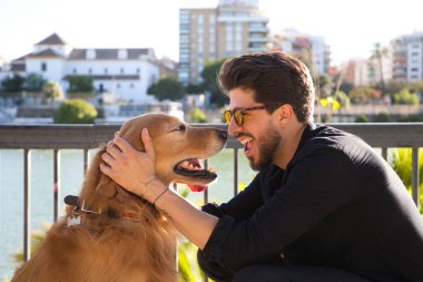 young latino man with sunglasses and beard and his brown golden retriever dog look at each other with love and affection. Concept pets, animals, dogs, love to retriever pets.