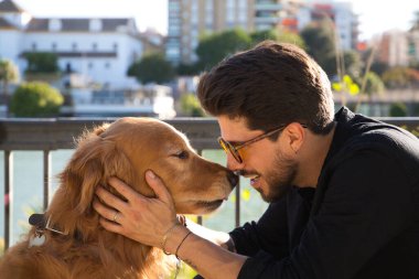 young latino man with sunglasses and beard and his brown golden retriever dog look at each other with love and affection. Concept pets, animals, dogs, love to retriever pets.