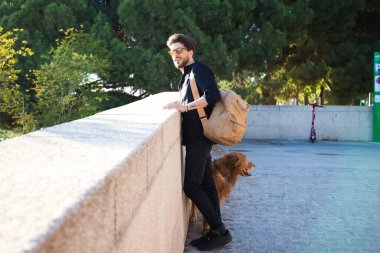 Golden retriever köpeğiyle yakışıklı genç bir adam duvara yaslanmış akşam güneşinin batışını seyrediyor. Evcil hayvanlar, hayvanlar, köpekler, evcil hayvanlar.