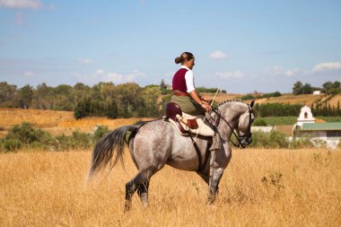 Young and beautiful Spanish woman on a Thoroughbred horse riding in the countryside in Spain. The woman is wearing a horse riding uniform. Thoroughbred and equine concept.