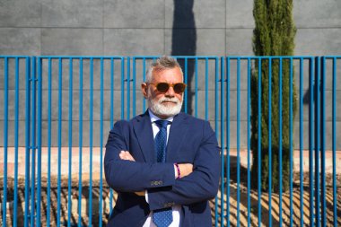Handsome, mature, grey-haired man with beard, jacket and tie and sunglasses is on the university campus where he works as a university lecturer. Concept professor, university rector.