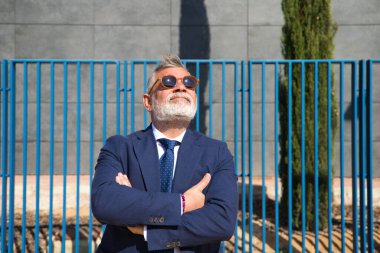 Handsome, mature, grey-haired man with beard, jacket and tie and sunglasses is on the university campus where he works as a university lecturer. Concept professor, university rector.