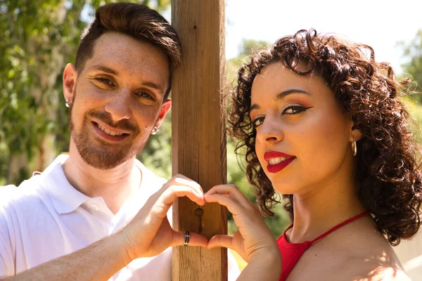 couple of latin lovers leaning on a wooden poster forming a heart with their hands. The man is camouflaging the woman to make her fall in love. They are bachata dancers. Latin dance concept.