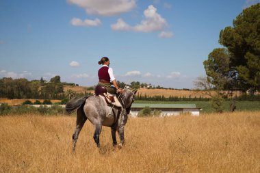 Young and beautiful Spanish woman on a Thoroughbred horse riding in the countryside in Spain. The woman is wearing a horse riding uniform. Thoroughbred and equine concept.