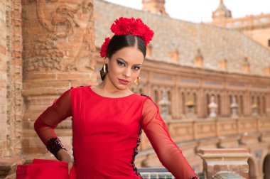 Beautiful teenage woman dancing flamenco on the balcony of a square in Seville. She wears a red dress with ruffles with a lot of art. Flamenco cultural heritage of humanity.