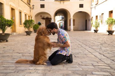 Genç Latin adam ve kahverengi Golden Retriever köpeği birbirlerine sevgi ve sevgi göstergesi olarak başlarını yan yana dikerlerken yerde diz çökerler. Evcil hayvanlar, hayvanlar, köpekler, evcil hayvanlar.