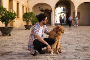young handsome Hispanic man with his brown golden retriever dog, they are crouched down looking at the same place. Concept pets, animals, dogs, pet love, golden retriever.