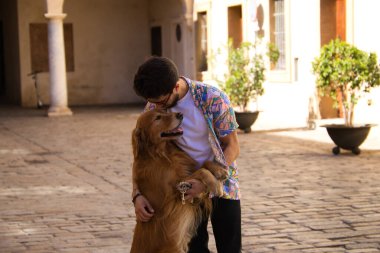 young latino man and his brown golden retriever dog walking in the street. The man kisses the dog on the head with affection. Concept pets, animals, dogs, pet love, golden retriever.