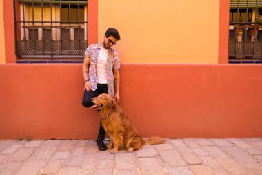 young latin man and his brown golden retriever dog, the man standing up looks at his pet who is sitting on the ground and grabs his head. Pets concept.