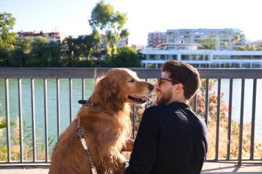 young latino man with sunglasses and beard and his brown golden retriever dog look at each other with love and affection. Concept pets, animals, dogs, love to retriever pets.