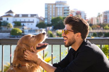 young latino man with sunglasses and beard and his brown golden retriever dog look at each other with love and affection. Concept pets, animals, dogs, love to retriever pets.