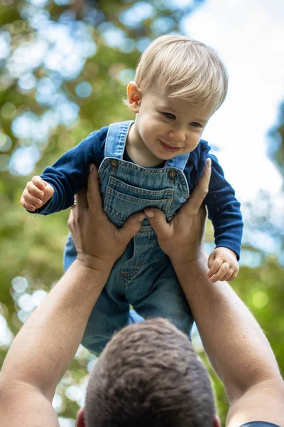 Küçük sarı saçlı çocuk doğada oturuyor ve gülüyor..