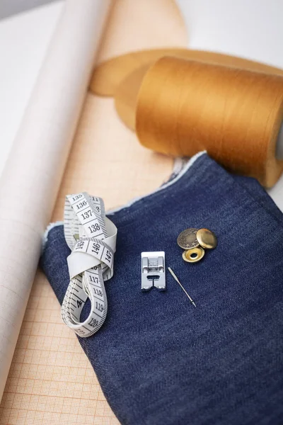Denim fabric for sewing and sewing items - tailoring curve including pin, skein of thread, paper for sewing pattern.
