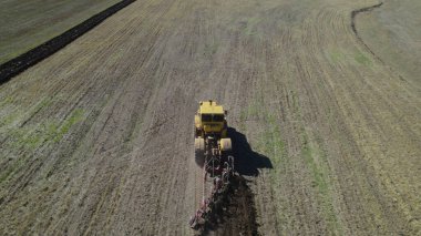 Tarlalarda çalışan sarı traktör.