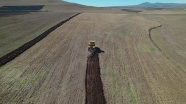 Tarlalarda çalışan sarı traktör.