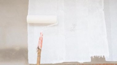 Hand with Paint Roller Moves on the Wall. Roller Painting gray Wall with White Paint. House Renovation Concept