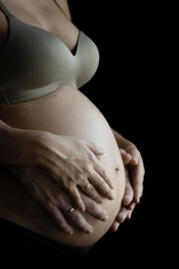 Karnına dokunan hamile bir kadının alyansını takan iki elin yakın duruşu..