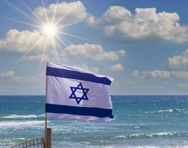 以色列国旗在阳光下飘扬 背景是多云的天空和大海 以色列独立日的概念 Yom Haatzmaut 挥动着桅杆在风中飘扬的以色列国旗 国家标志 复制空间 — 图库照片