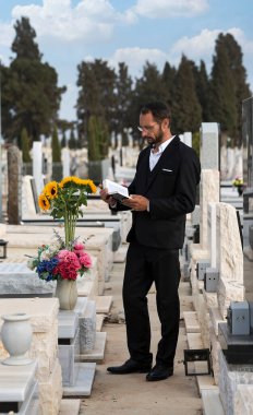 İsrail 'de bir Yahudi mezarlığında dua etmek. Sığ bir alan derinliğine sahip Yahudi mezar taşları. Seçici odaklanma. Ormandaki eski Yahudi mezarlığı. Siyah kippah içindeki sakallı Yahudi İbrani İncili okuyup dua ediyor..