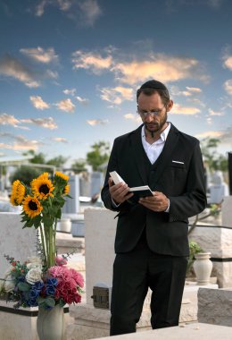 Siyah kippah içinde sakallı Yahudi İbrani İncili okuyup dua ediyor. İsrail 'de bir Yahudi mezarlığında dua etmek. Seçici odaklanma. Ormandaki eski Yahudi mezarlığı. Hasidik Yahudi Tevrat okuyor. Dikey yönelim