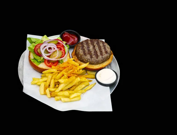 Good Isolated on black background of hamburger with ingredients: french fries and vegetables. Copy space for your text. Fresh, hearty grilled hamburger with fries, salad, onion and tomato. Fast food