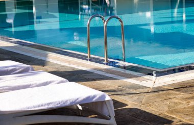 Yüzme havuzuna inmek için merdiven paslanmaz tırabzanlar ve beyaz havluları olan güzel plaj sandalyeleri. Güneş doğarken demir korkuluklar ve mavi su. Açık hava yüzme havuzuna giriyor. Yaz