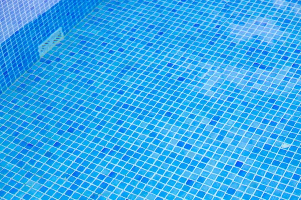Clear water of swimming pool with mosaic bottom. Blue marble mosaic tile texture background. Swimming pool bottom caustics ripple and flow. Underwater shot of blue glass tiles on pool bottom. Close up
