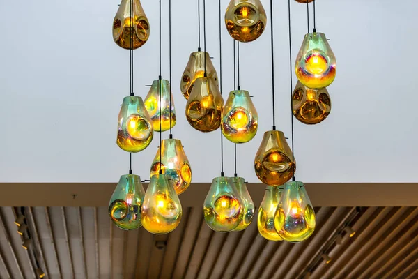 Rain drop glass pendant lights hanging from the ceiling. Ceiling glass balls living room interior decoration. Light bulb glowing hanging in rows on long wires, cords. Lighting lamps on the chandelier