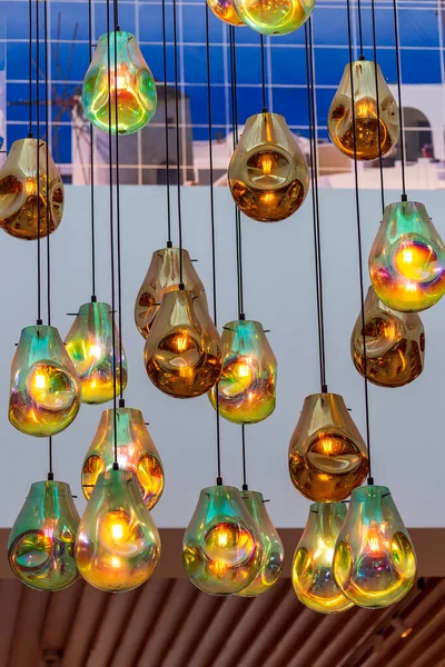 Vertical shot of rain drop glass pendant lights hanging from the ceilings. Abstract Modern Chandelier. Ceiling glass balls living room interior. Light bulb glowing hanging in rows on long wires, cords