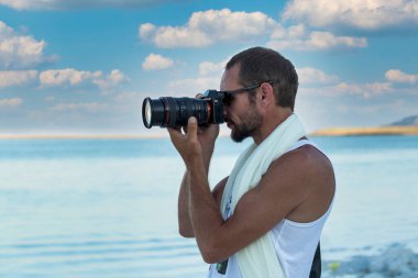 Man photographer takes photographs with dslr camera at the beach. Travel, vacations, professional freelance work, active lifestyle concept. Handsome muscular man using picture with modern camera