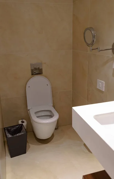 Contemporary interior of empty deluxe restroom. Close up of open toilet bowl in room. White ceramic clean toilet bowl near brown wall in modern home. Perspective of men or women restroom, wc.