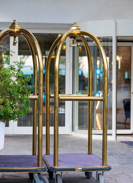 Luggage trolley cart for carrying baggage on front entrance to a hotel background. Empty metal suitcases cart used for travel bags ready to check in into hotel. Summer holiday, traveling, vacation.