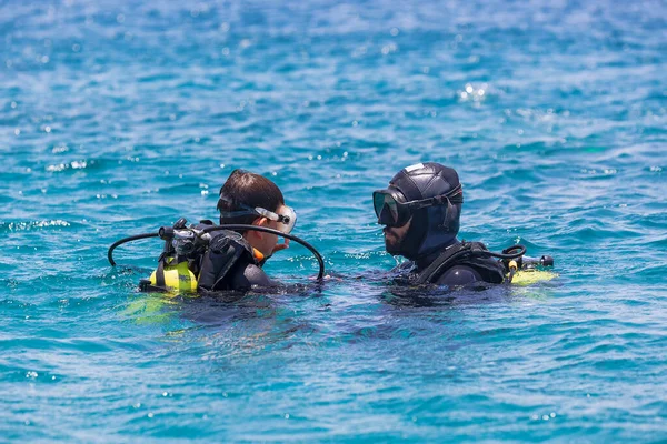 Instructor giving scuba diving lessons to a kid. Scuba diving Instructor teaching a little boy to dive. Diver course. Two scuba divers in shallow Red Sea. Divers dressed in diving suit, aqualung.