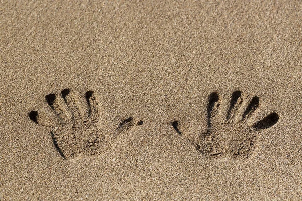 Human handprint on sand at the sandy beach. Palm print. Closeup shot of handprints in the sand as nice nature summer background. Two hand prints on beige sea sand texture. Top view with copy space